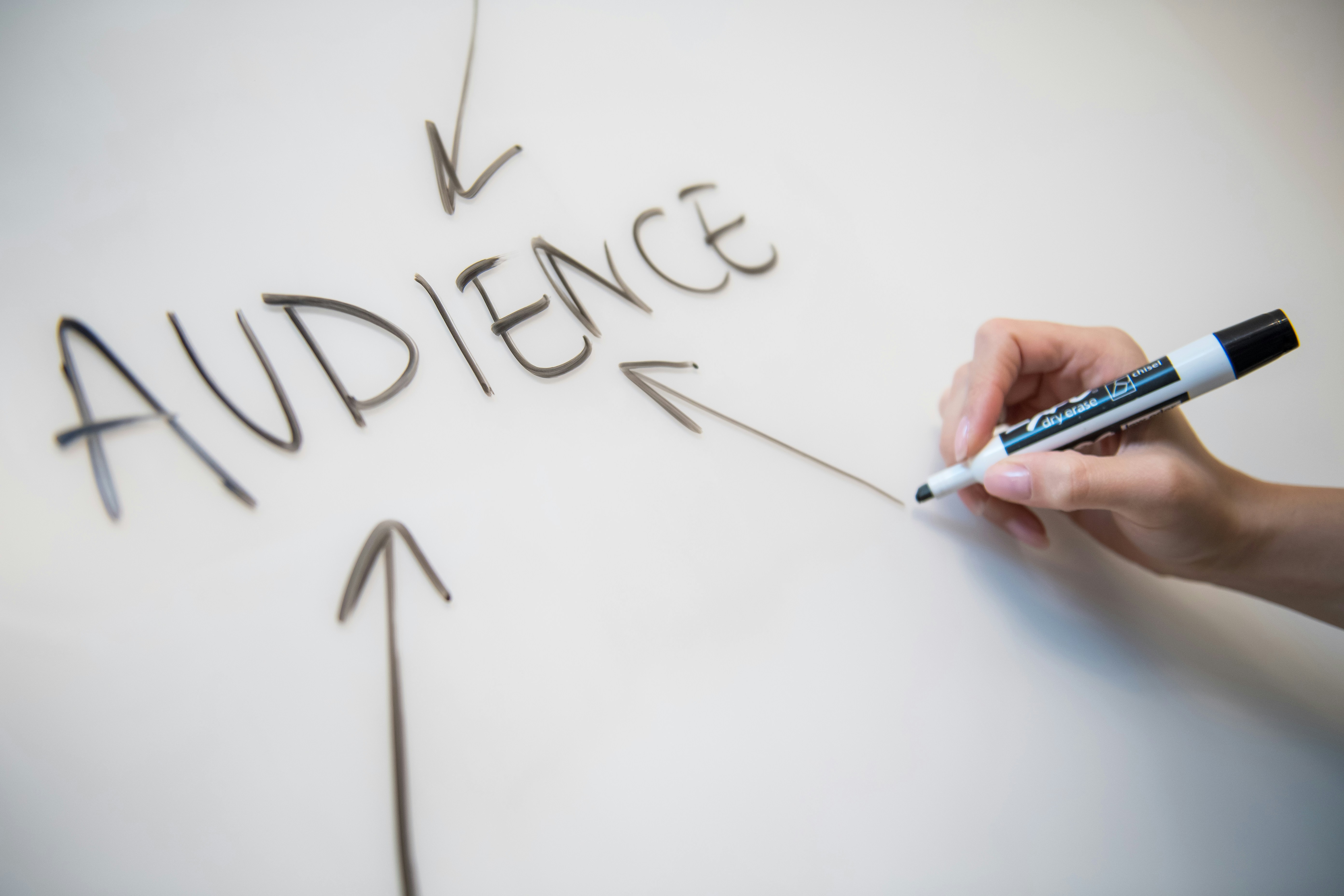 A person writing on a white board the word "Audience" with arrows pointing at it!