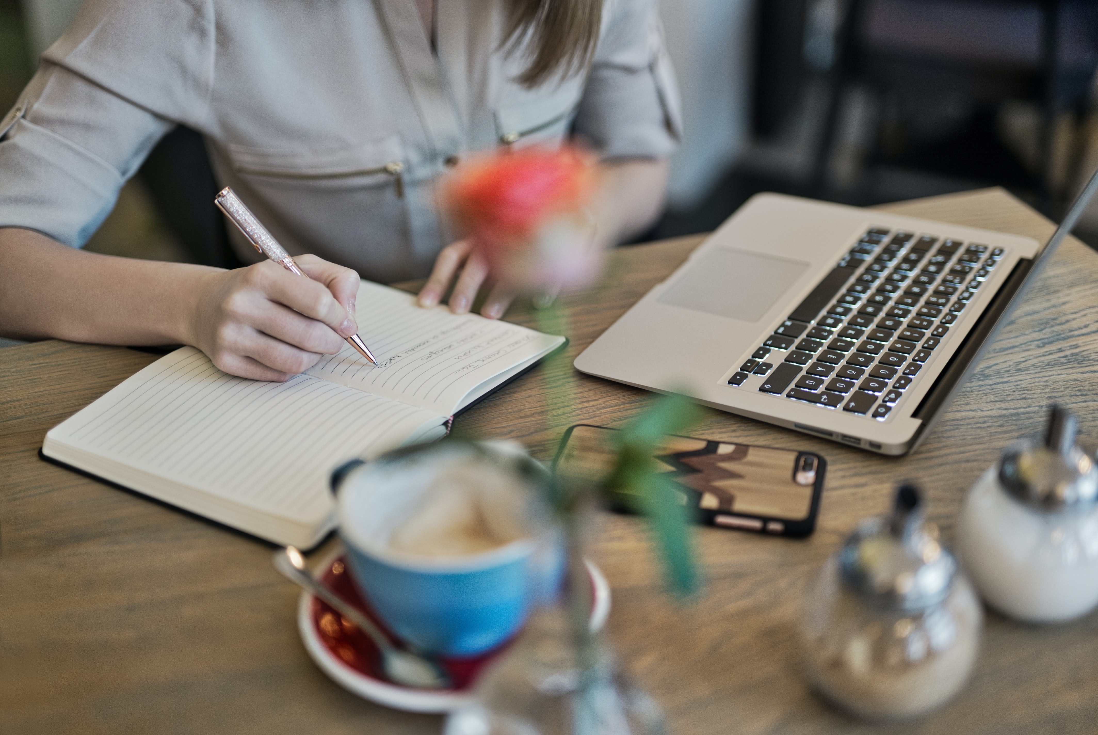A girl writing her goals on a notebook, having a laptop in front of her