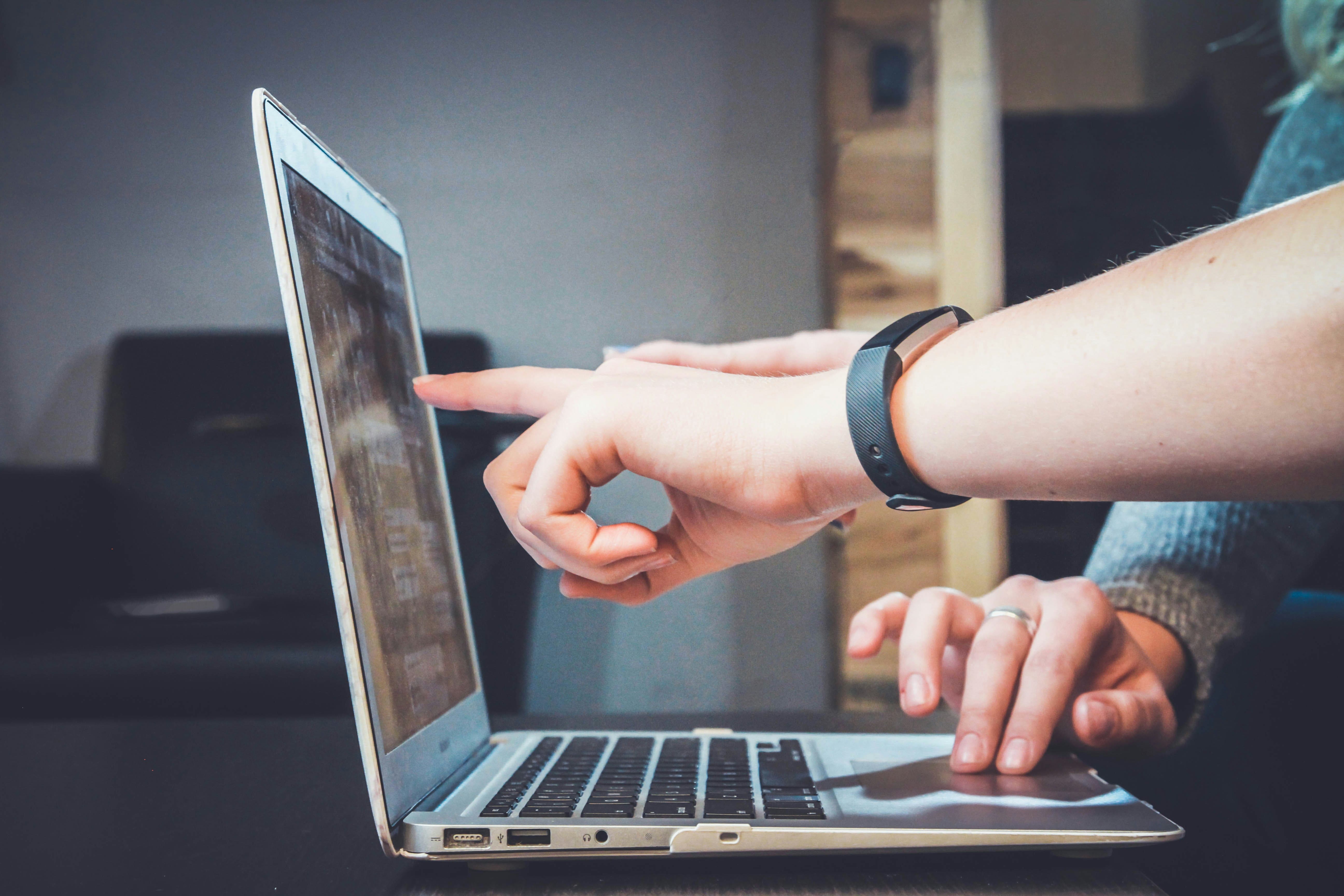A person pointing at the laptop screen, and another touching the laptop touchpad